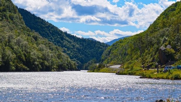 Green tree-lined mountain ranges lining the glimmering river within the Adirondacks on a sunny day