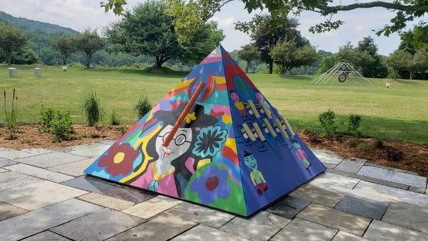 Colorful pyramid amid the artpark percussion garden in front of a green field surrounded by trees on a semi cloudy day