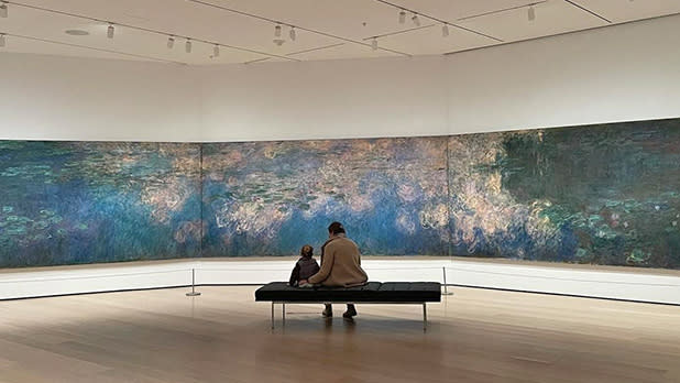 An adult and child sit on a bench in front of artwork at MoMA