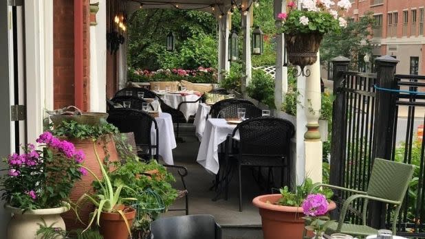 A terrace with restaurant tables, purple flowers and green plants