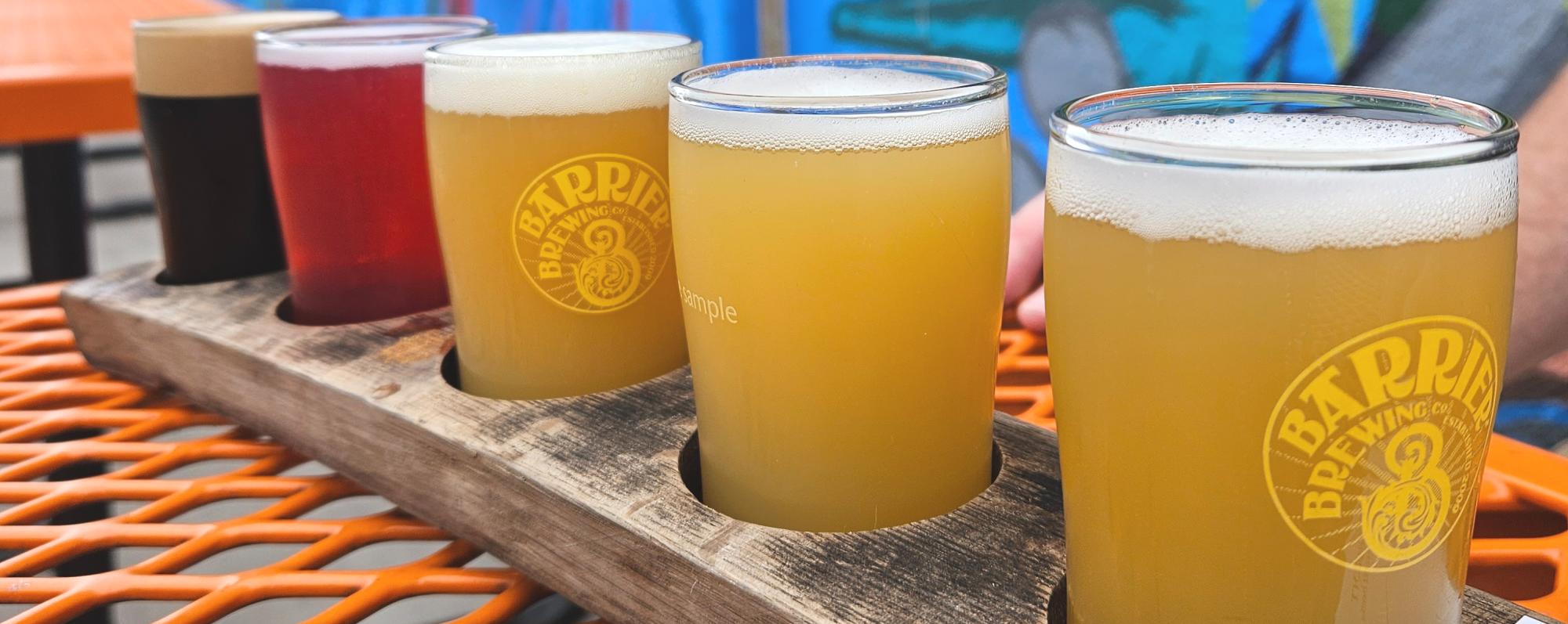 A flight of beers on a table in front of a graffiti wall outside Barrier Brewing Co.