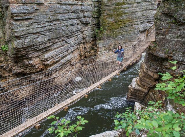 A person walks on a bridge between rocks in Ausable Chasm