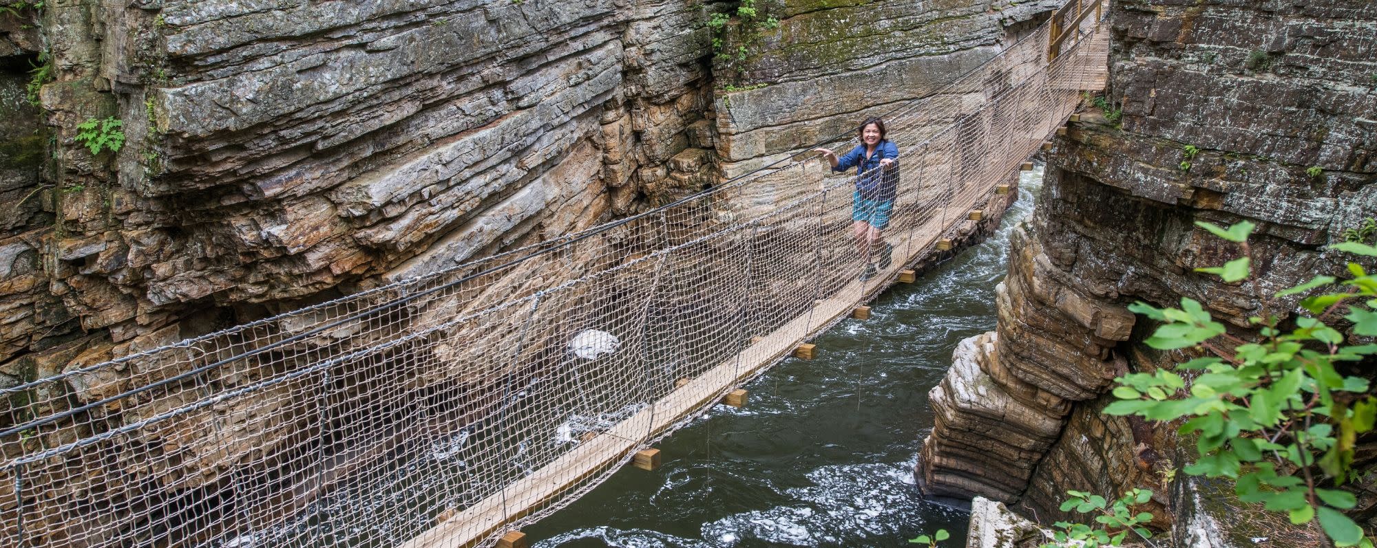 A person walks on a bridge between rocks in Ausable Chasm