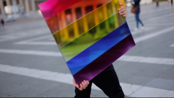 Mirrored glass reflecting the rainbow flag in an urban landscape