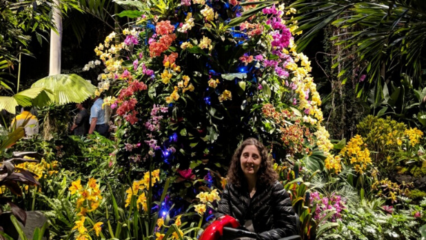 A woman poses in her wheelchair in front of orchids at the orchid show at the New York Botanical Gardens in the Bronx.