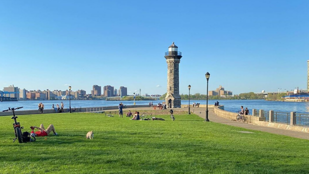 People laying on the grass with the Roosevelt Island Lighthouse in the background on a sunny day in NYC